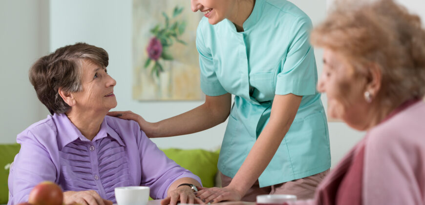 two women in assisted living talking with their nursing aid at table