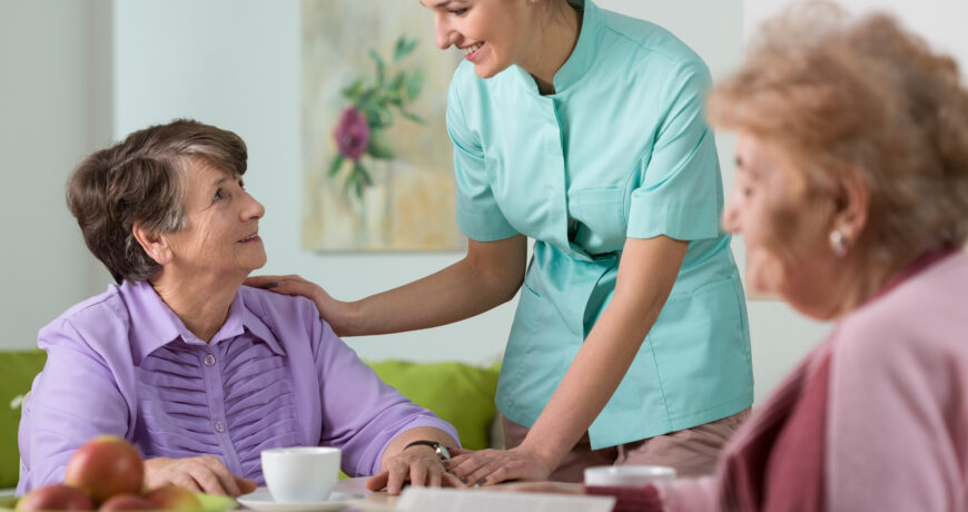 two women in assisted living talking with their nursing aid at table